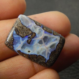 May include: A rectangular, polished opal gemstone. The stone features a dark brown matrix speckled with gold, framing a vibrant display of blue, white, and iridescent colors. The opal's surface showcases a unique pattern of veins and color play.