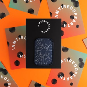 May include: A black patch with a white starburst design on a blue background. The patch is surrounded by cards with the text "I AM TIRED OF EARTH" in a circle.