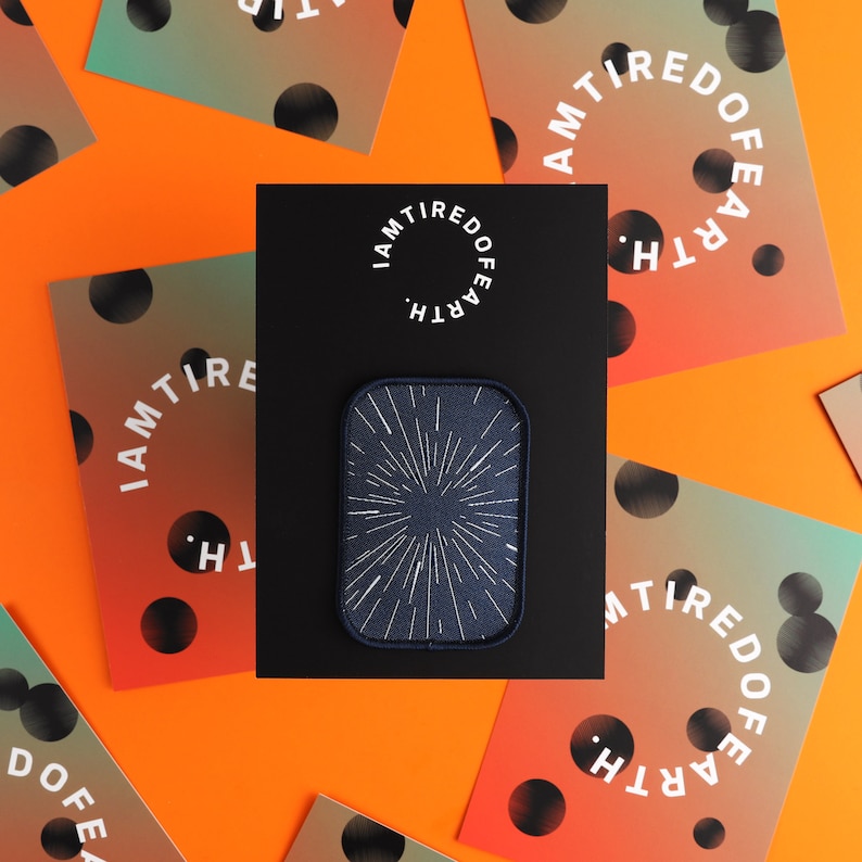 May include: A black patch with a white starburst design on a blue background. The patch is surrounded by cards with the text "I AM TIRED OF EARTH" in a circle.