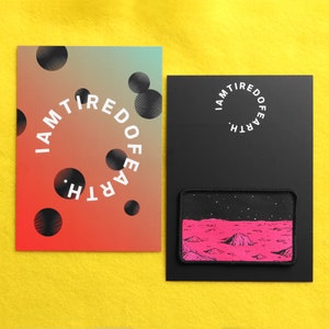 May include: Two black cards with white text that reads "I am tired of earth". One card has a gradient background with black circles. The other card has a black background with a pink and black patch depicting a landscape with stars.