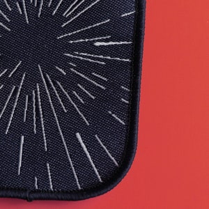 May include: A black fabric patch with a white starburst design. The patch has a stitched edge.