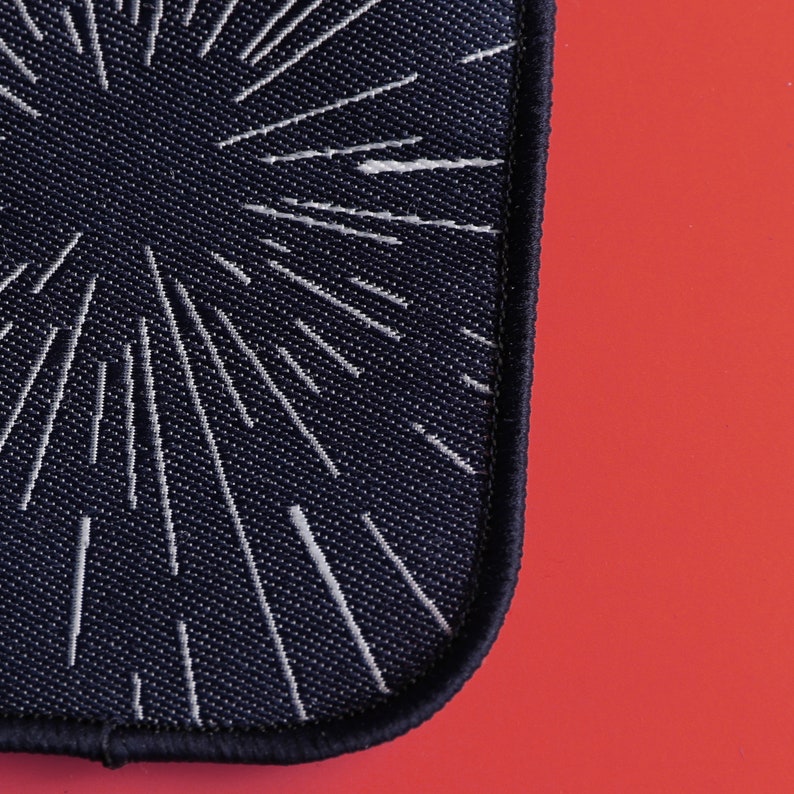 May include: A black fabric patch with a white starburst design. The patch has a stitched edge.
