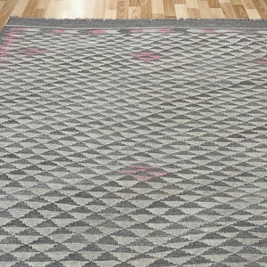 May include: A grey and white geometric patterned rug with pink accents. The rug has a diamond pattern with a subtle texture.