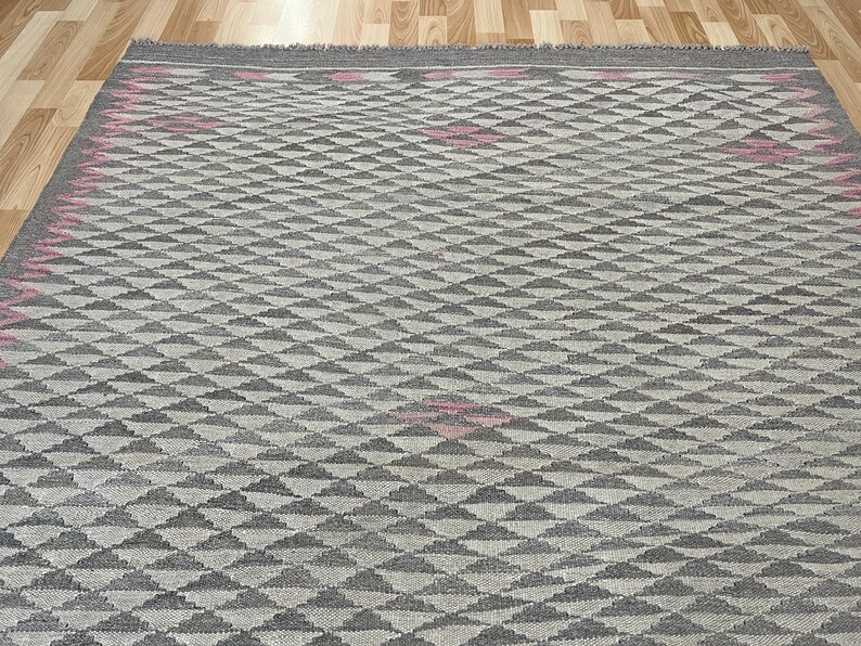May include: A grey and white geometric patterned rug with pink accents. The rug has a diamond pattern with a subtle texture.