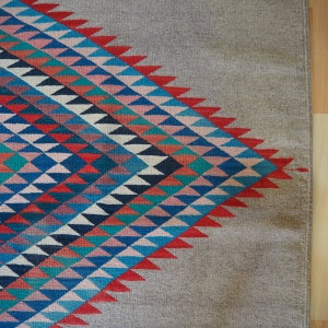 May include: A rug with a geometric pattern of triangles in shades of blue, red, pink, and white. The pattern is on a beige background.