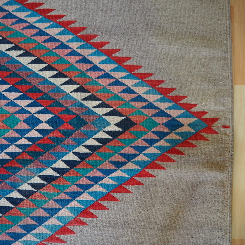 May include: A rug with a geometric pattern of triangles in shades of blue, red, pink, and white. The pattern is on a beige background.