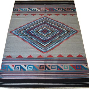 May include: A gray and white rug with a large diamond pattern in shades of blue, red, green, and pink. The diamond pattern is surrounded by a border of geometric designs in the same colors.