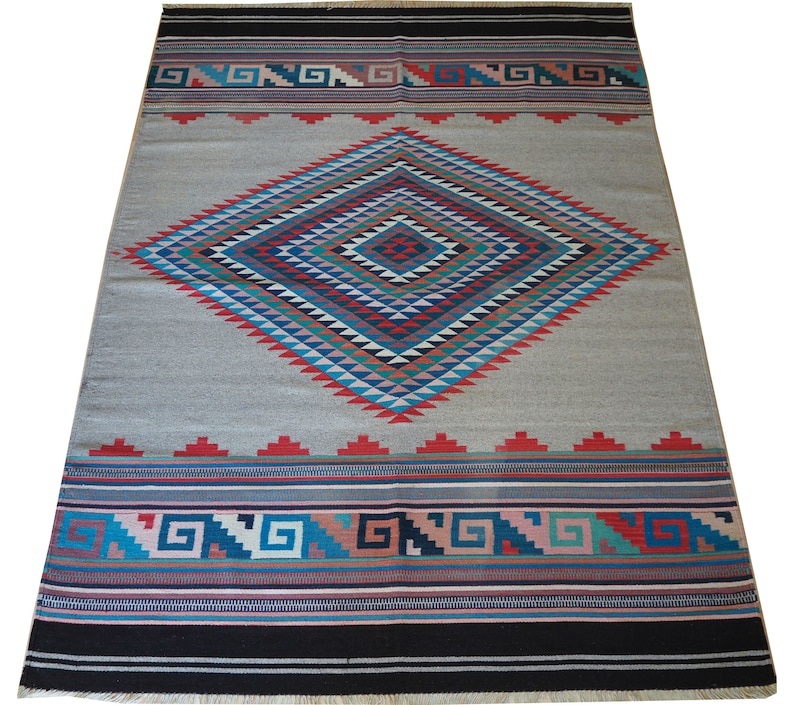 May include: A gray and white rug with a large diamond pattern in shades of blue, red, green, and pink. The diamond pattern is surrounded by a border of geometric designs in the same colors.