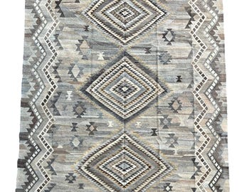 May include: A gray and beige rug with a geometric pattern of diamonds and triangles. The rug has a fringe border.