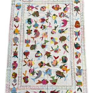 May include: A white rug with a colorful fish design. The fish are embroidered in various colors, including red, blue, green, yellow, and pink. The rug has a white background and a border of colorful swirls.