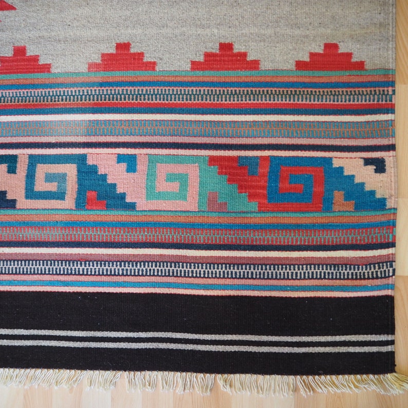 May include: A colorful woven rug with a geometric pattern in shades of red, blue, green, and brown. The rug has a fringe border.