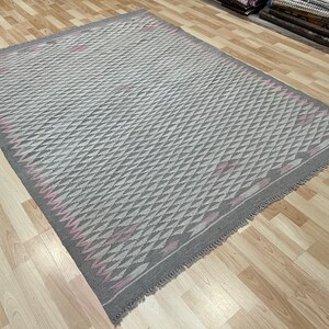 May include: A grey and pink patterned rug with a geometric design. The rug has a fringed edge.