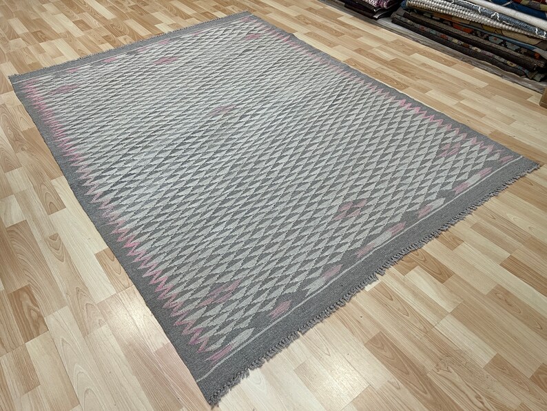 May include: A grey and pink patterned rug with a geometric design. The rug has a fringed edge.