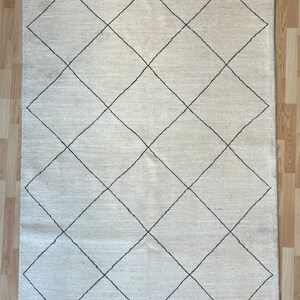 May include: A white rug with a diamond pattern in black. The rug has a simple, modern design.