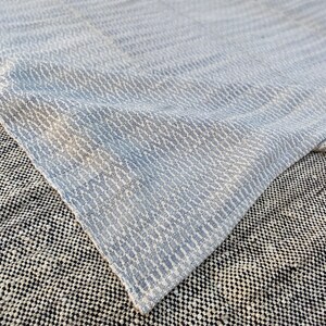May include: A white and light blue patterned rug with a subtle wave design. The rug is folded in half and the bottom half is laying on a black and white patterned rug.