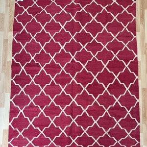 Puede incluir: Una alfombra roja con un patrón geométrico blanco. El patrón está formado por cuadrados y diamantes que se repiten.