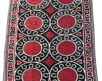 May include: A black and red textile rug with a repeating pattern of circles and floral designs. The rug has a white border.