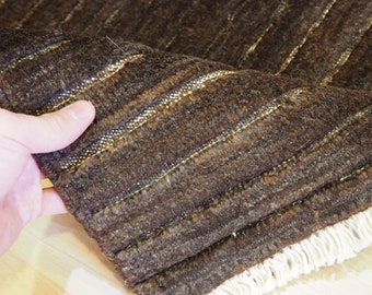 Puede incluir: Primer plano de una alfombra de rayas marrones y beige con flecos blancos. La alfombra está hecha de un material suave y texturizado.