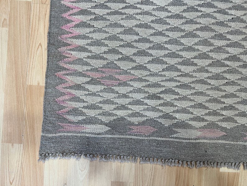 May include: A grey and pink woven rug with a geometric pattern. The rug has a fringed border.