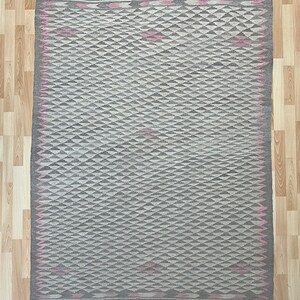 May include: A grey and white geometric patterned rug with a pink border. The rug has a diamond pattern with a subtle sheen.
