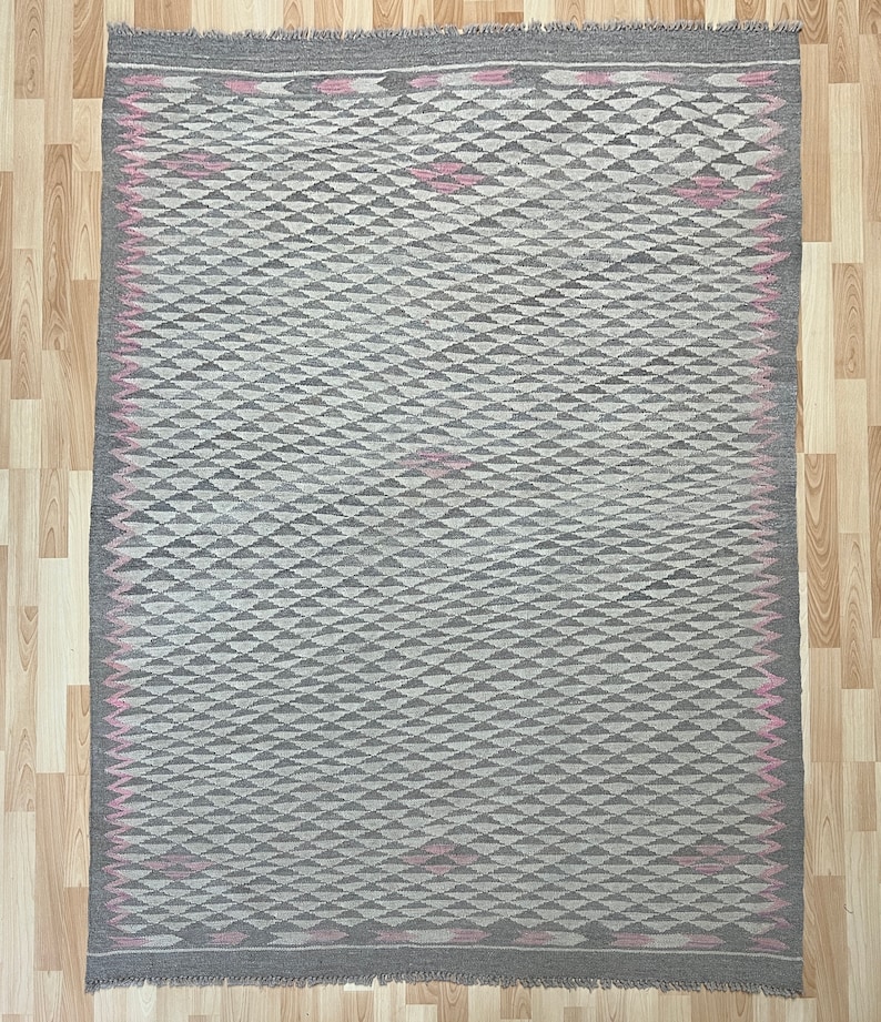 May include: A grey and white geometric patterned rug with a pink border. The rug has a diamond pattern with a subtle sheen.