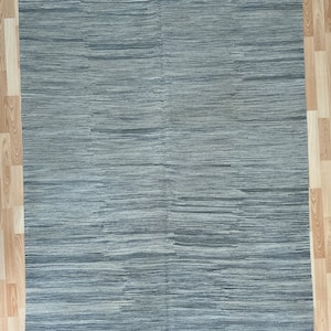 Può includere: Un tappeto a strisce grigio e bianco con un leggero luccichio. Il tappeto ha un bordo a frangia ed è realizzato in materiale tessuto.
