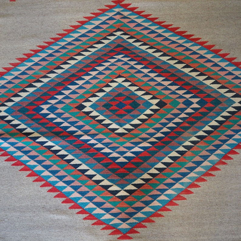 May include: A Navajo rug with a geometric pattern of red, blue, green, and white triangles. The rug is woven with a diamond shape in the center.