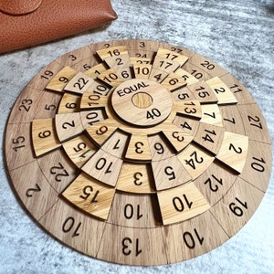 May include: A circular wooden puzzle with a central circle labelled "EQUAL" and the number "40". The puzzle is made up of multiple pieces, each with a number on it. The numbers on the pieces range from 2 to 27.