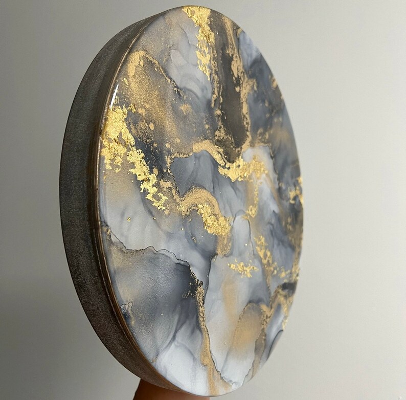 May include: Round, gray and white resin art piece with gold accents. The art piece has a swirling, abstract design.