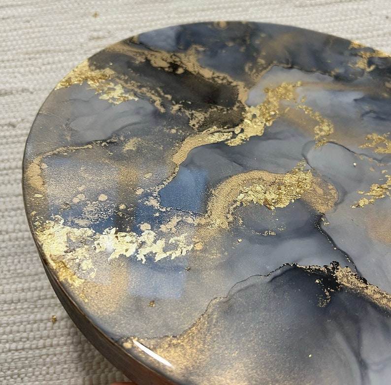 May include: A round, gray and black resin coaster with gold flecks. The coaster has a marbled, abstract design.