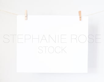 May include: A white blank card with rounded corners is hanging from a string with two wooden clothespins. The card is on a white background. The text "STEPHANIE ROSE STOCK" is printed in gray on the card.