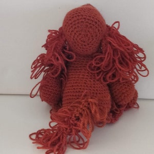 May include: A crocheted red plush toy shaped like a dog with long, shaggy hair. The toy has a simple face with no eyes or mouth.