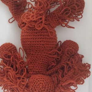 May include: A crocheted stuffed animal in the shape of a dog. The dog is brown and has long, shaggy fur. The dog is lying on its back with its legs in the air.