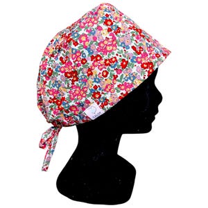 Peut inclure: Un bonnet de bloc fleuri avec un motif de fleurs rouges, roses, bleues et jaunes sur fond blanc. Le bonnet est noué à l'arrière et porte une petite étiquette avec le mot "CALOT".