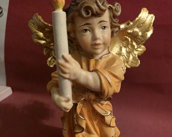 May include: A detailed figurine of an angel holding a candle. The angel is dressed in a flowing orange robe with gold trim and has golden wings. The candle has a realistic flame.
