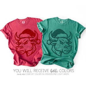 May include: Two t-shirts, one crimson and one light green, each featuring a bull graphic wearing a Santa hat. The text "YOU WILL RECEIVE both COLORS" is at the bottom of the image. The shirts are Comfort Colors.