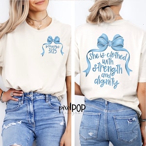 May include: A white t-shirt with a blue bow and the text "Proverbs 31:25" on the front. The back of the shirt has a larger blue bow with the text "She is clothed with strength and dignity".