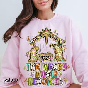 Peut inclure: Sweat-shirt rose avec un graphique coloré d'une scène de la nativité et le texte "The Weary World Rejoices".
