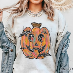 May include: A white t-shirt with a glittery orange pumpkin with a black outline and bats. The pumpkin has a black glitter face with a wide smile and eyes.