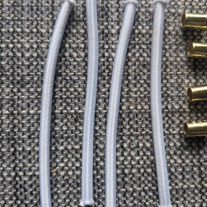 May include: Five white elastic bands, each about 10 inches long, are laid out on a gray textured surface. The elastic bands are all the same size and shape, and they are all made of a soft, stretchy material.
