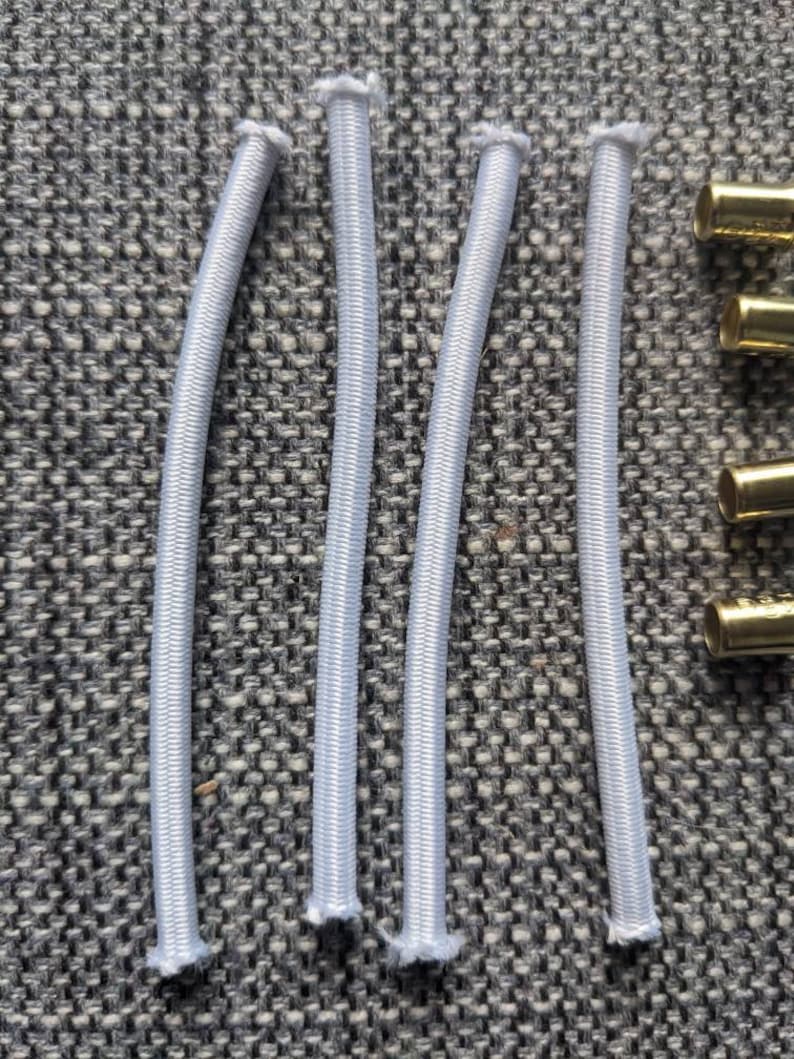May include: Five white elastic bands, each about 10 inches long, are laid out on a gray textured surface. The elastic bands are all the same size and shape, and they are all made of a soft, stretchy material.