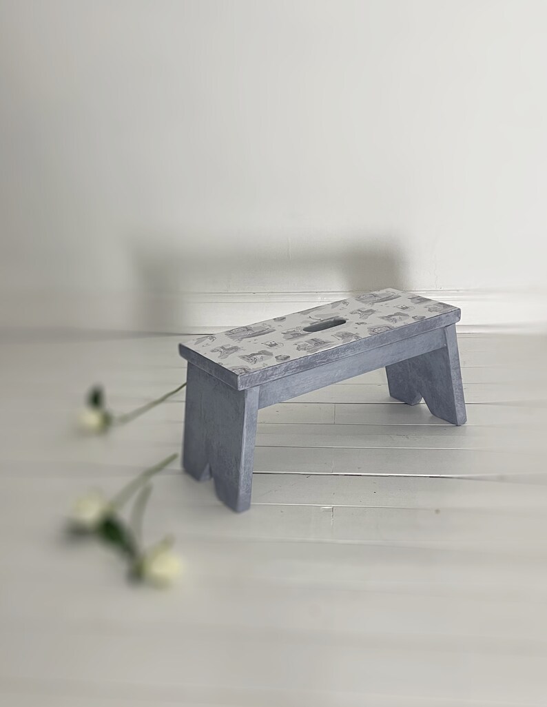 Peut inclure: Un petit tabouret en bois gris avec un dessus &agrave; motifs. Le tabouret a un design simple avec un dessus rectangulaire et quatre pieds.