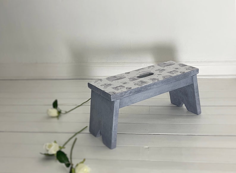 Peut inclure: Un petit tabouret en bois gris avec un dessus &agrave; motifs blancs et gris. Le tabouret est pos&eacute; sur un sol en bois blanc.