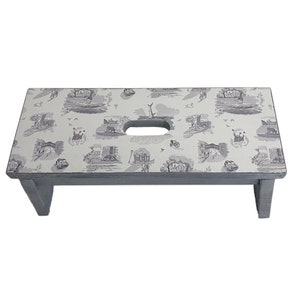 Peut inclure: Un tabouret en bois gris avec un dessus blanc orn&eacute; d'un motif r&eacute;p&eacute;titif d'illustrations noires et blanches. Le dessus a une poign&eacute;e d&eacute;coup&eacute;e.