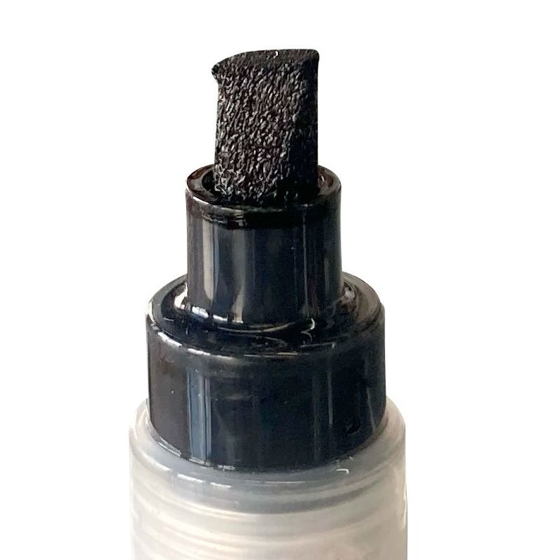 Op de afbeelding: Close-up van een zwarte marker met een viltpunt. De marker zit in een doorzichtige plastic fles met een zwarte dop.
