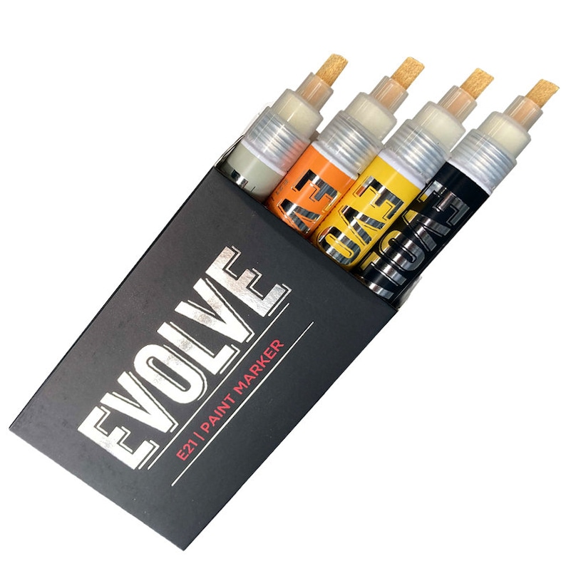 Op de afbeelding: Een set van vier verfmarkeringen in een zwarte doos. De markeringen zijn gelabeld "Evolve E21" en zijn in de kleuren zilver, oranje, geel en zwart.