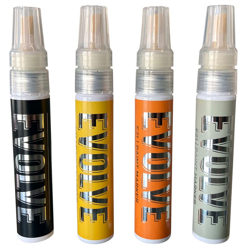 Op de afbeelding: Vier verfmarkers met zilveren opschrift "EVOLVE" aan de zijkant. De markers zijn zwart, geel, oranje en grijs.