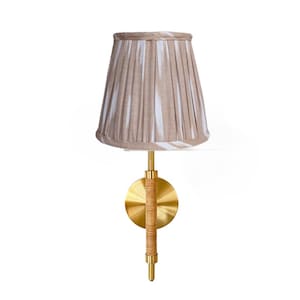 May include: A wall-mounted lamp with a pleated lampshade in beige and white vertical stripes. The lamp features a brass base and a woven rattan detail on the stem. The lamp is designed for indoor use.