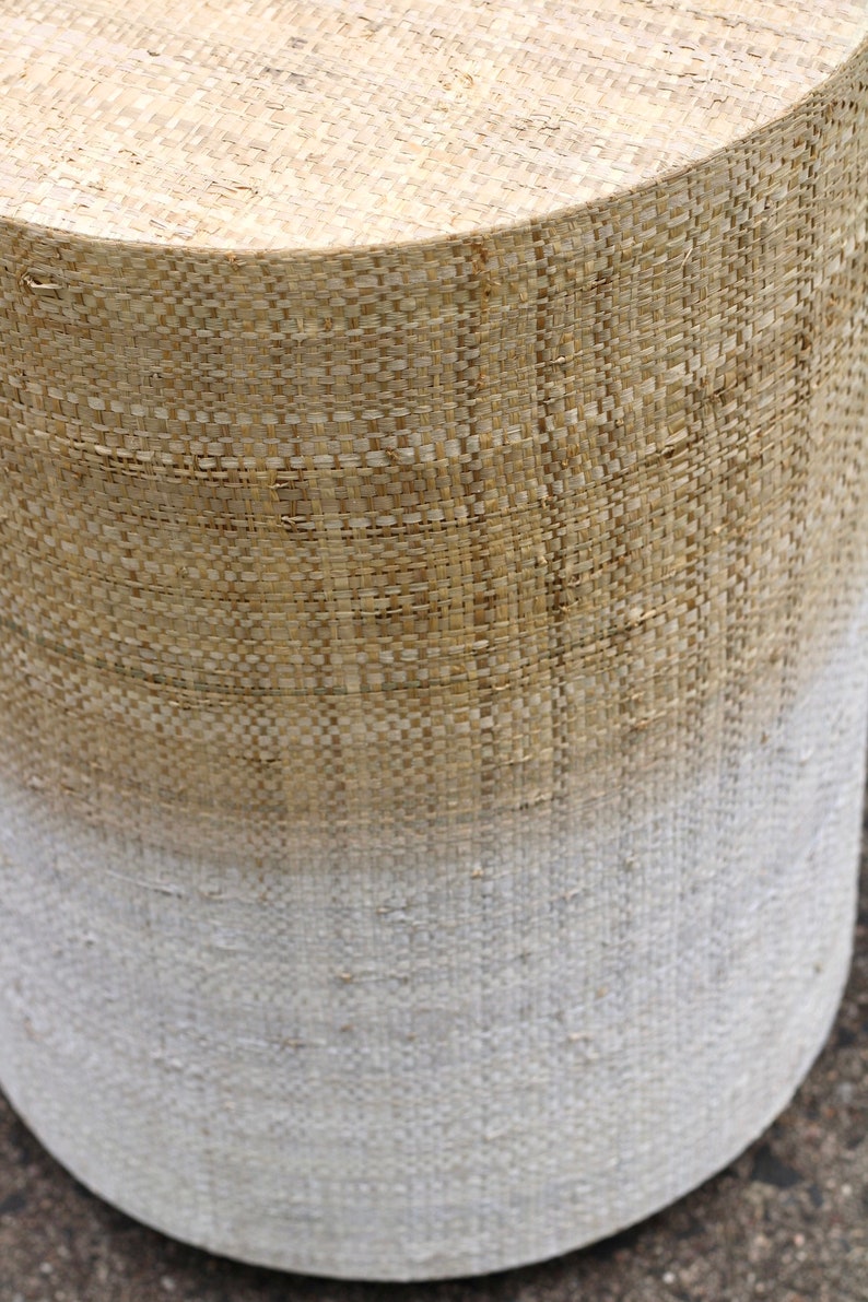 May include: A woven cylindrical stool with a natural brown top and a white bottom, creating an ombre effect.
