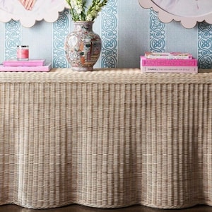 Könnte beinhalten: Ein weißer Korb-Konsolentisch mit einer wellenförmigen Basis. Der Tisch ist mit einer Vase mit weißen Blumen, zwei Büchern und einer Kerze dekoriert. Der Hintergrund ist eine blau-weiße gemusterte Tapete.